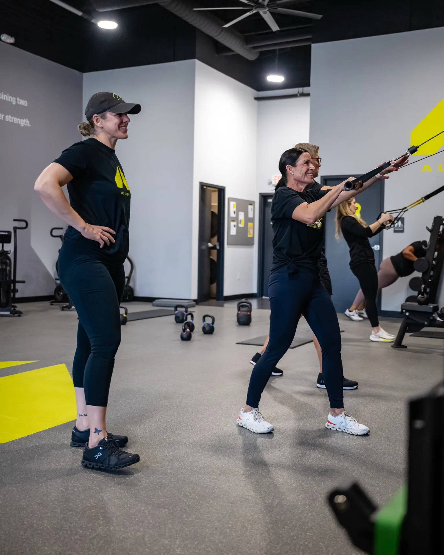 A trainer oversees two members doing suspension-strap pulls during a small group session at Alloy Colorado Springs