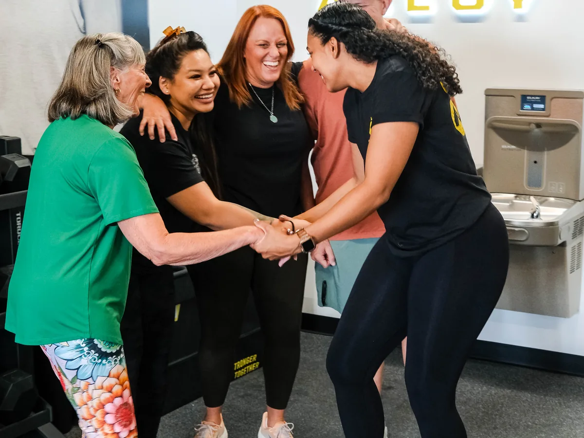 Members share a laugh in a team huddle at Alloy Personal Training Colorado Springs